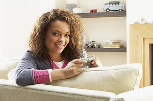 Woman Looking At Pictures On Digital Camera Relaxing Sitting On Sofa At Home 