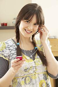 Woman Listening To MP3 Player On Headphones Relaxing Sitting On Rug At Home 