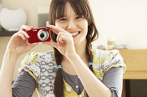 Young Woman Taking Photograph On Digital Camera At Home 