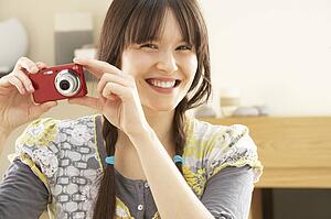 Young Woman Taking Photograph On Digital Camera At Home 