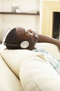 Young Man Relaxing Sitting On Sofa Listening to Music At Home On Headphones