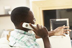 Young Man Relaxing Sitting On Sofa At Home Talking On Phone