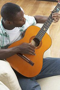 Young Man Relaxing Sitting On Sofa Playing Acoustic Guitar