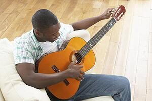 Young Man Relaxing Sitting On Sofa Playing Acoustic Guitar