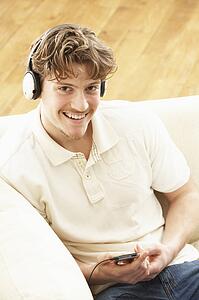 Man Listening To MP3 Player On Headphones Relaxing Laying On Rug At Home 