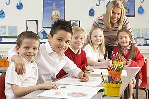 Group Of Primary Schoolchildren And Teacher Working At Desks In Classroom
