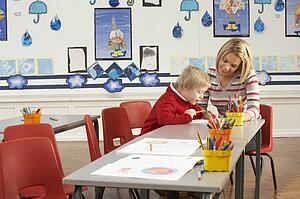 Male Primary School Pupil And Teacher Working At Desk In Classroom