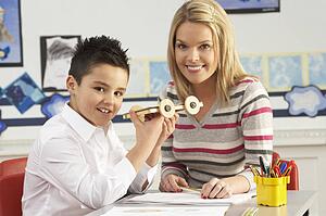 Male Primary School Pupil And Teacher Working At Desk In Classroom