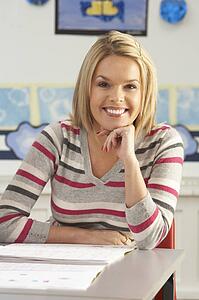 Portrait Of Female Teacher Sitting At Desk In Classroom