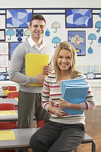 Portrait Of Male And Female Teacher Sitting At Desk In Classroom