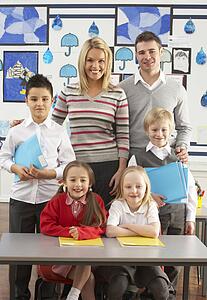 Portrait Of Group Of Primary Schoolchildren And Teachers Sitting At Desk In Classroom