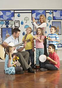 Teachers Playing Guitar With Pupils Having Music Lesson In Classroom
