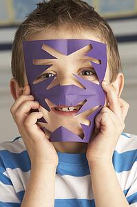 Male Primary School Pupil Cutting Out Paper Shapes In Craft Lesson