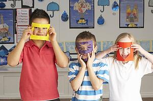 Group Of Primary School Children Cutting Out Paper Shapes In Craft Lesson