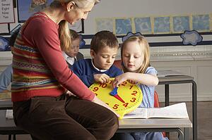 Female Teacher In Primary School Teaching Children To Tell Time In Classroom