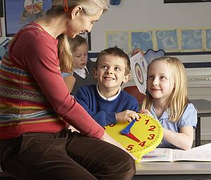 Female Teacher In Primary School Teaching Children To Tell Time In Classroom