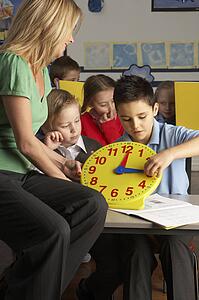 Female Teacher In Primary School Teaching Children To Tell Time In Classroom
