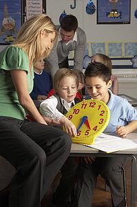 Female Teacher In Primary School Teaching Children To Tell Time In Classroom