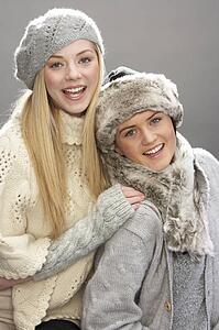 Two Fashionable Teenage Girls Wearing Cap And Knitwear In Studio In Front Of Christmas Tree