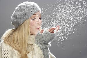 Teenage Girl Wearing Warm Winter Clothes And Hat Blowing Snow In Studio
