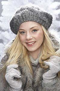 Fashionable Teenage Girl Wearing Cap And Fur Coat In Studio In Front Of Christmas Tree