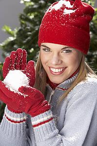 Fashionable Teenage Girl Wearing Cap And Knitwear Holding Snowball In Studio In Front Of Christmas Tree