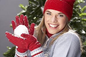 Fashionable Teenage Girl Wearing Cap And Knitwear Holding Snowball In Studio In Front Of Christmas Tree