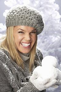 Fashionable Woman Wearing Cap And Knitwear Holding Snowball In Studio In Front Of Christmas Tree
