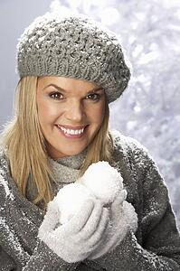 Fashionable Woman Wearing Cap And Knitwear Holding Snowball In Studio In Front Of Christmas Tree