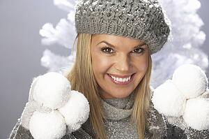Fashionable Woman Wearing Cap And Knitwear Holding Snowball In Studio In Front Of Christmas Tree