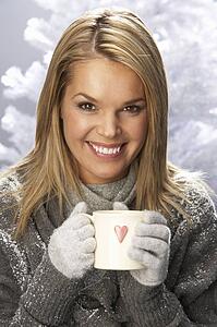 Young Woman Drinking Hot Drink Wearing Knitwear In Studio In Front Of Christmas Tree