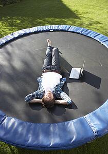 Young Man Relaxing On Trampoline With Laptop