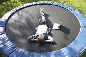 Young Man Relaxing On Trampoline With Laptop