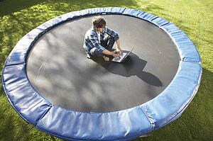 Young Man Relaxing On Trampoline With Laptop