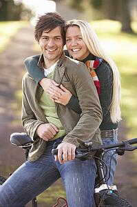 Portrait Of Young Couple With Cycle In Autumn Park