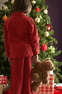 Young Girl Standing With Teddy Bear In Front Of Christmas Tree