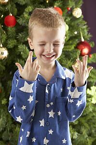 Young Boy Crossing Fingers In Front Of Christmas Tree