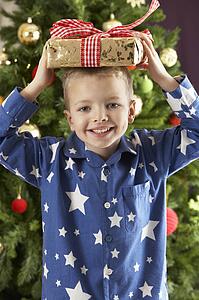 Young Boy Holding Wrapped Present In Front Of Christmas Tree