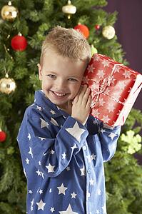 Young Boy Holding Wrapped Present In Front Of Christmas Tree