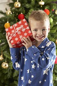 Young Boy Holding Wrapped Present In Front Of Christmas Tree
