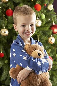 Young Boy Cuddling Teddy Bear In Front Of Christmas Tree