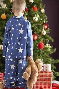 Young Boy Holding Teddy Bear In Front Of Christmas Tree