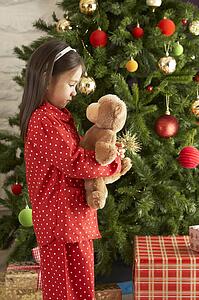 Young Girl Cuddling Teddy Bear In Front Of Christmas Tree
