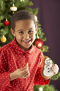 Young Boy Eating Cookie In Front Of Christmas Tree