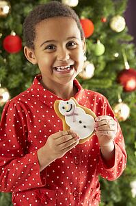 Young Boy Eating Cookie In Front Of Christmas Tree