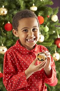 Young Boy Eating Mince Pie In Front Of Christmas Tree