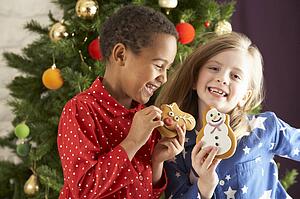 Two Young Children Eating Christmas Treats In Front Of Christmas Tree