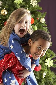 Two Young Children Having Fun In Front Of Christmas Tree