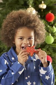 Young Boy Eating Cookie In Front Of Christmas Tree