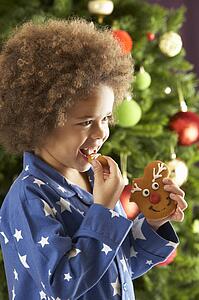 Young Boy Eating Cookie In Front Of Christmas Tree
